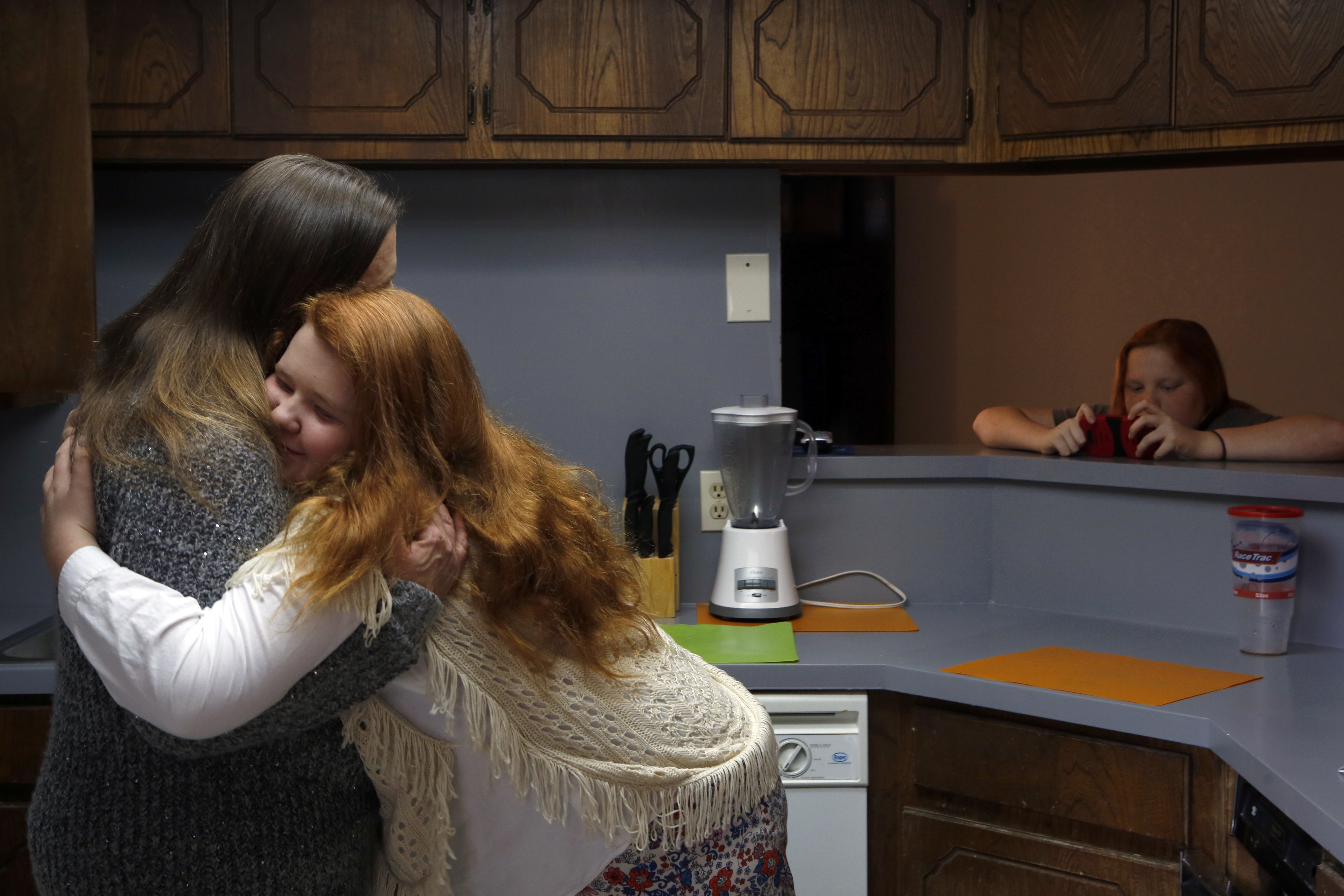 After three years staying in motels, the Rosenheim family just moved into a three-bedroom home where each child has their own bed. In the kitchen, Belinda gives her daughter Allison (14) a hug and Tony looks at his phone. (photo copyright Lara Solt)